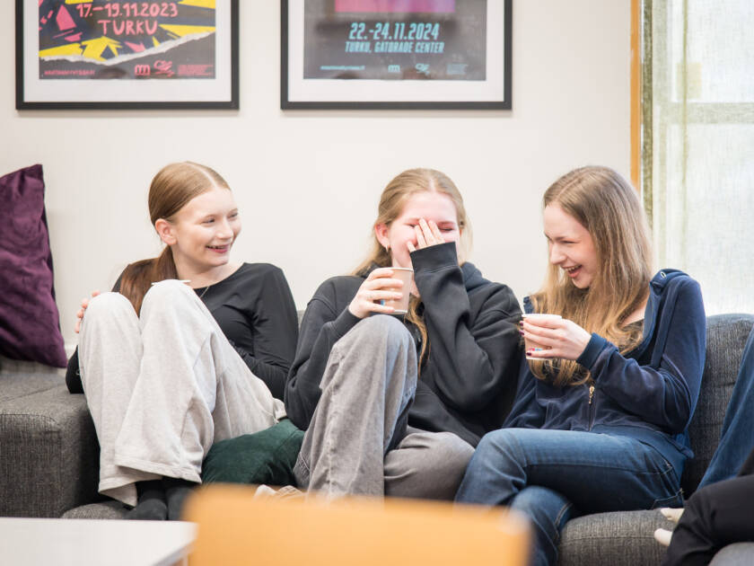 Kolme nuorta Kaarinan kirkon nuortentilan sohvalla, nauravat