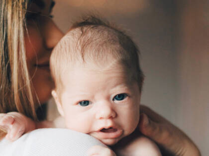En liten baby är på en kvinnas axel och tittar rakt in i kameran.