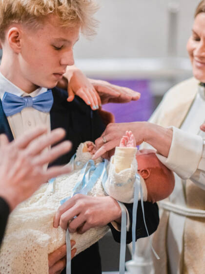 En präst och en grupp andra människor välsignar ett barn i dopkolt.