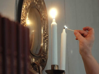 A hand lighting two candles at a church.