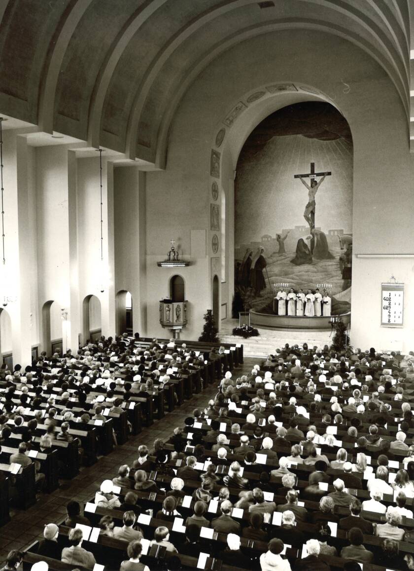 Suuri kirkko, jossa on täynnä ihmisiä. Alttarilla on ristiinnaulittu Jeesus ja papit, jotka johtavat jumalanpalvelusta.
