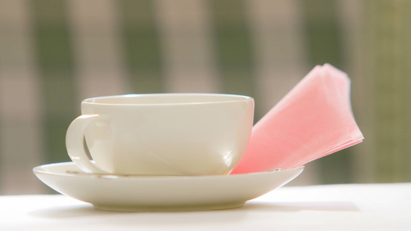 Kahvikuppi tassilla ja vaaleanpunaisella servetillä.