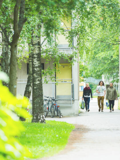 Kolme opiskelijaa kävelee kerrostalojen keskellä.