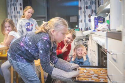 Tyttö ottaa pellillistä pipareita pois uunista. Muut lapset katsovat vieressä.