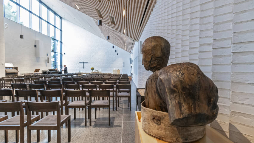 Kirkkosalissa penkkirivejä, puupatsas etualalla.