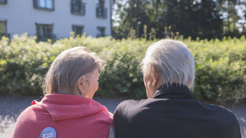 Kaksi eläkeläistä istuu auringonpaisteessa selkä kameraan päin.