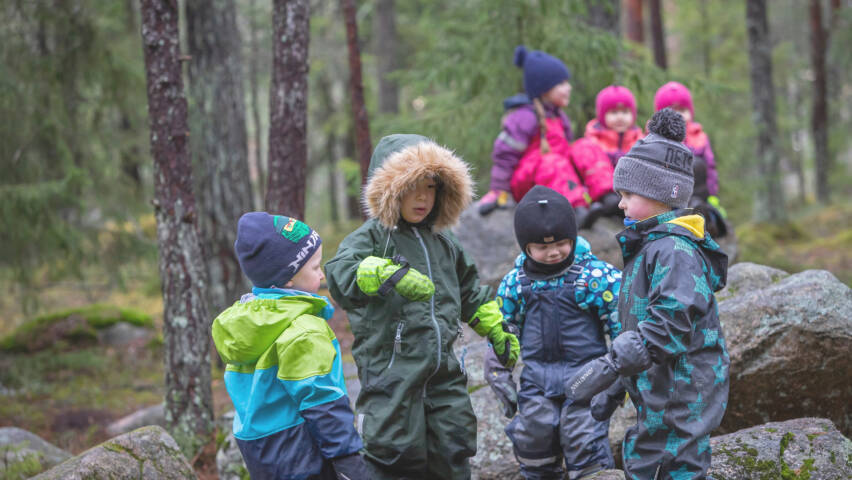Ryhmä lapsia leikkii sateisessa metsässä.