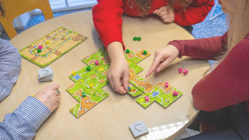 Kolme ihmistä pelaa Carcassone-lautapeliä.