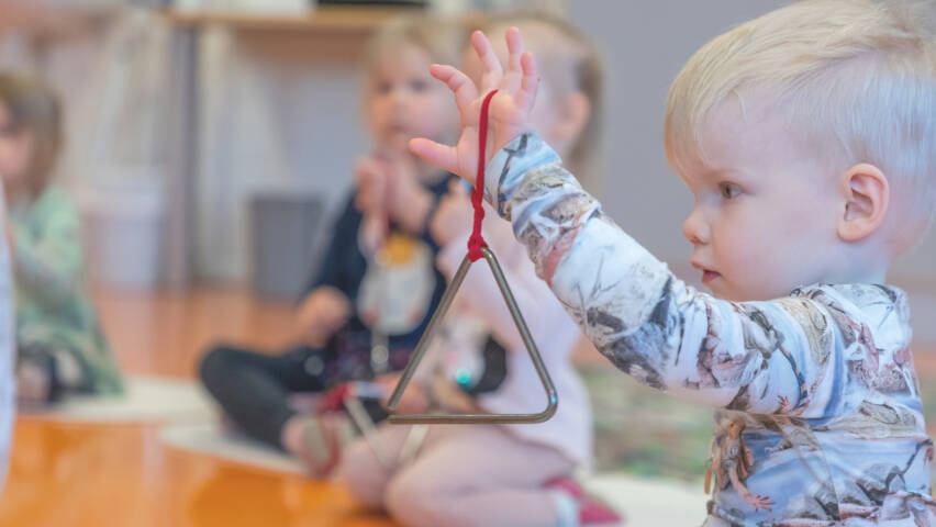 Taapero roikottaa triangelia edessään.