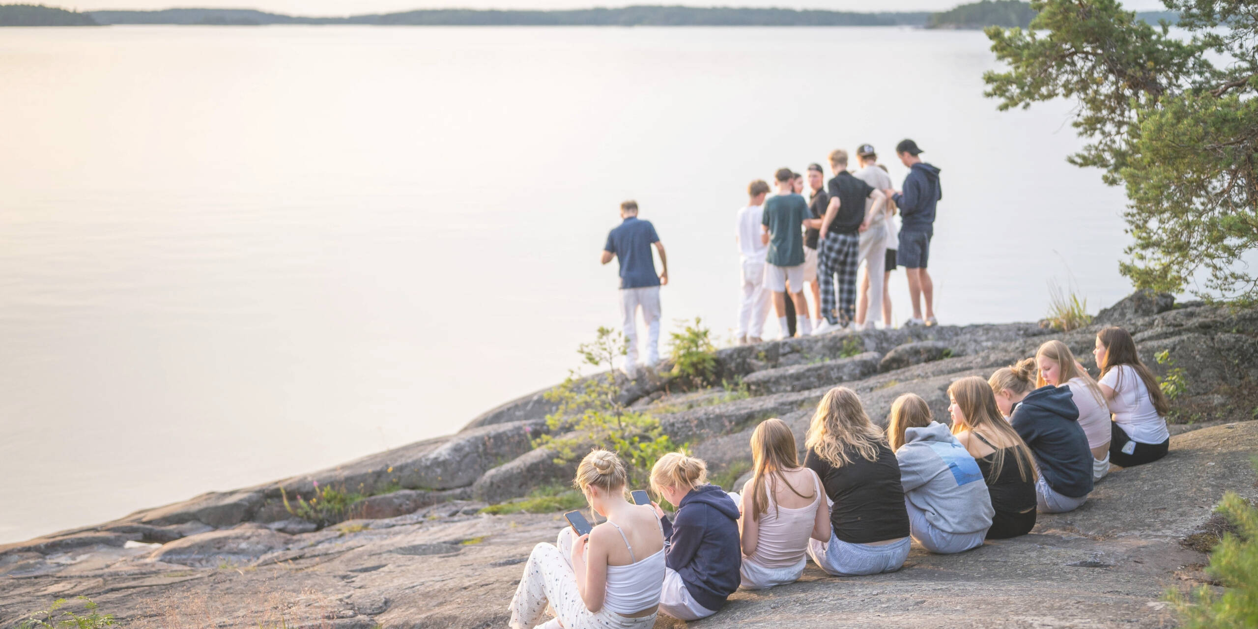 Iso määrä nuoria istuskelee ja seisoo rantakallioilla.