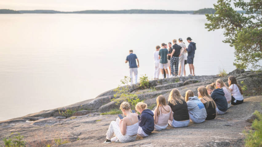 Iso määrä nuoria istuskelee ja seisoo rantakallioilla.