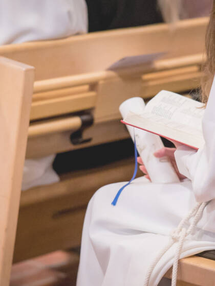 Nuori istuu kirkon penkissä alba päällä ja virsikirja kädessä.