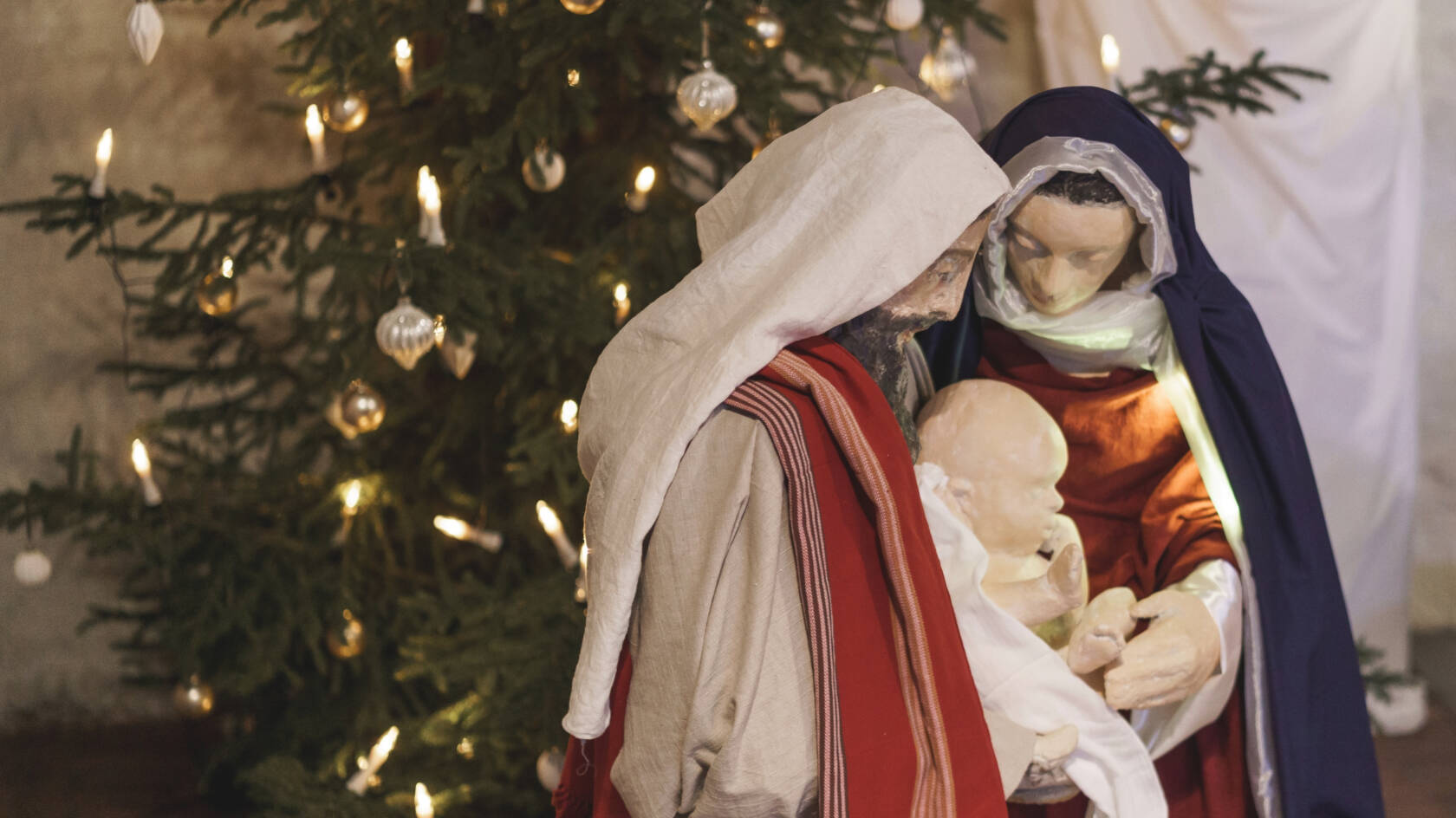 Suurikokoinen seimiasetelma, jossa on Maria, Joosef ja Jeesus-lapsi. Taustalla on joulukuusi.