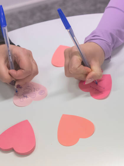 Kaksi kättä kirjoittaa sydämen muotoisiin post-it lappuihin.