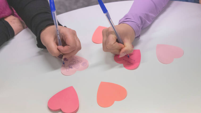 Två händer skriver på hjärtformade post-it-lappar.