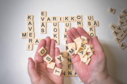 Kädet pitelevät aakkospelin palasia. Pöydälle on tehty sanat Varikko, kaveri, eväs, ruoka, me, sä ja usko.