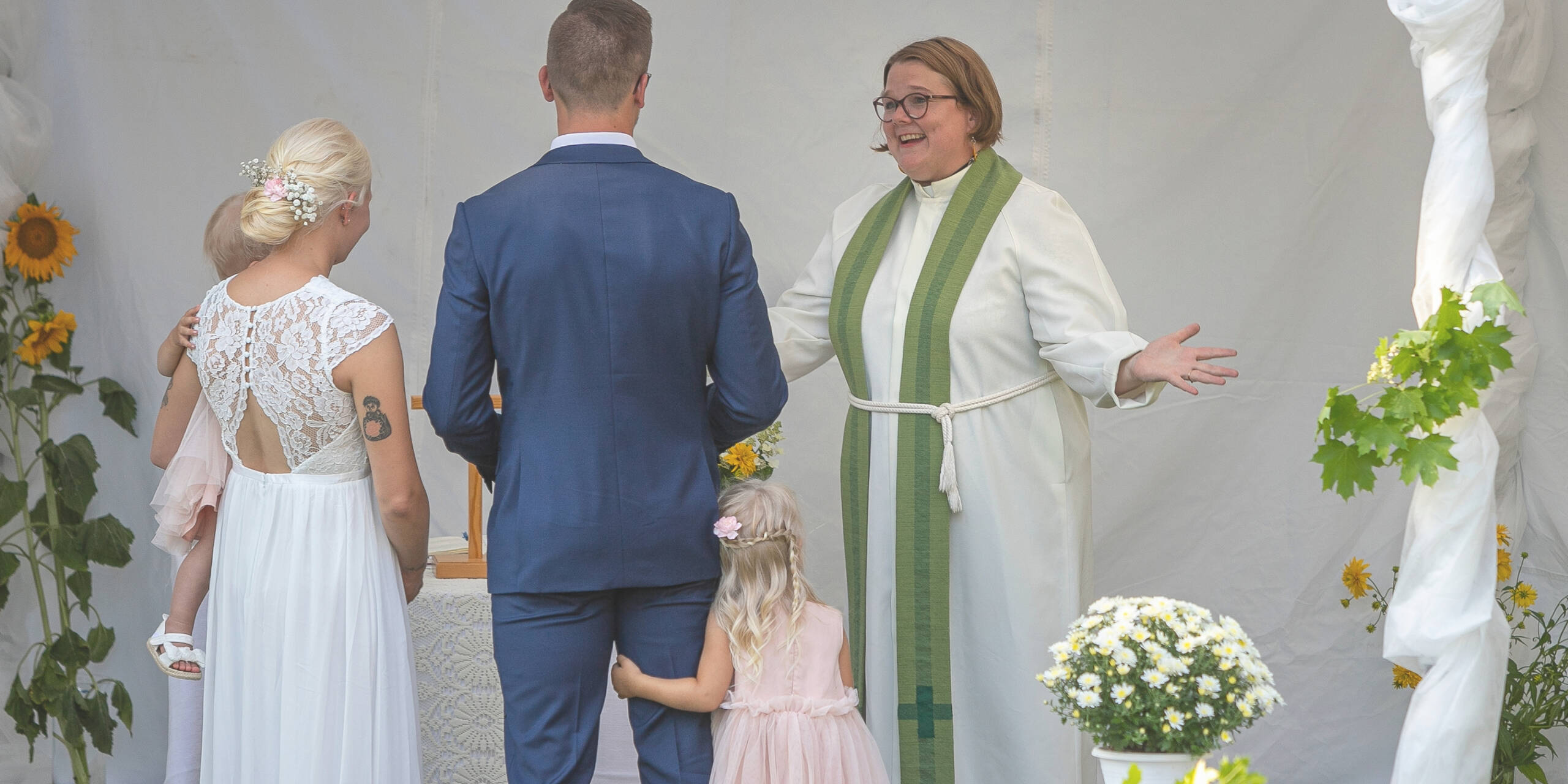 Pappi vastaanottaa hääparin kädet levitettynä avoimeksi.