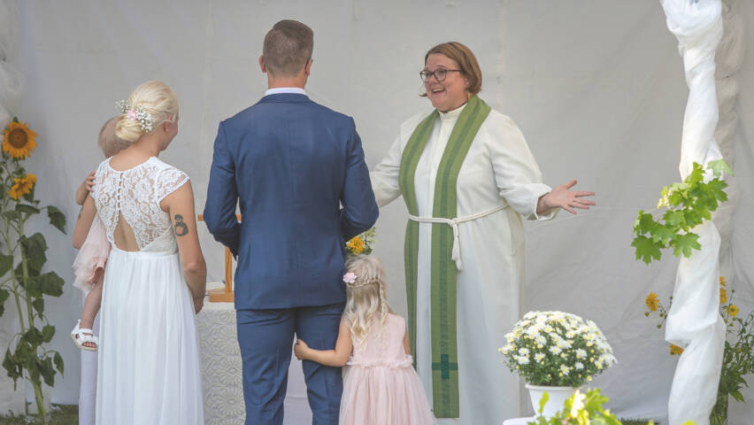 Pappi vastaanottaa hääparin kädet levitettynä avoimeksi.