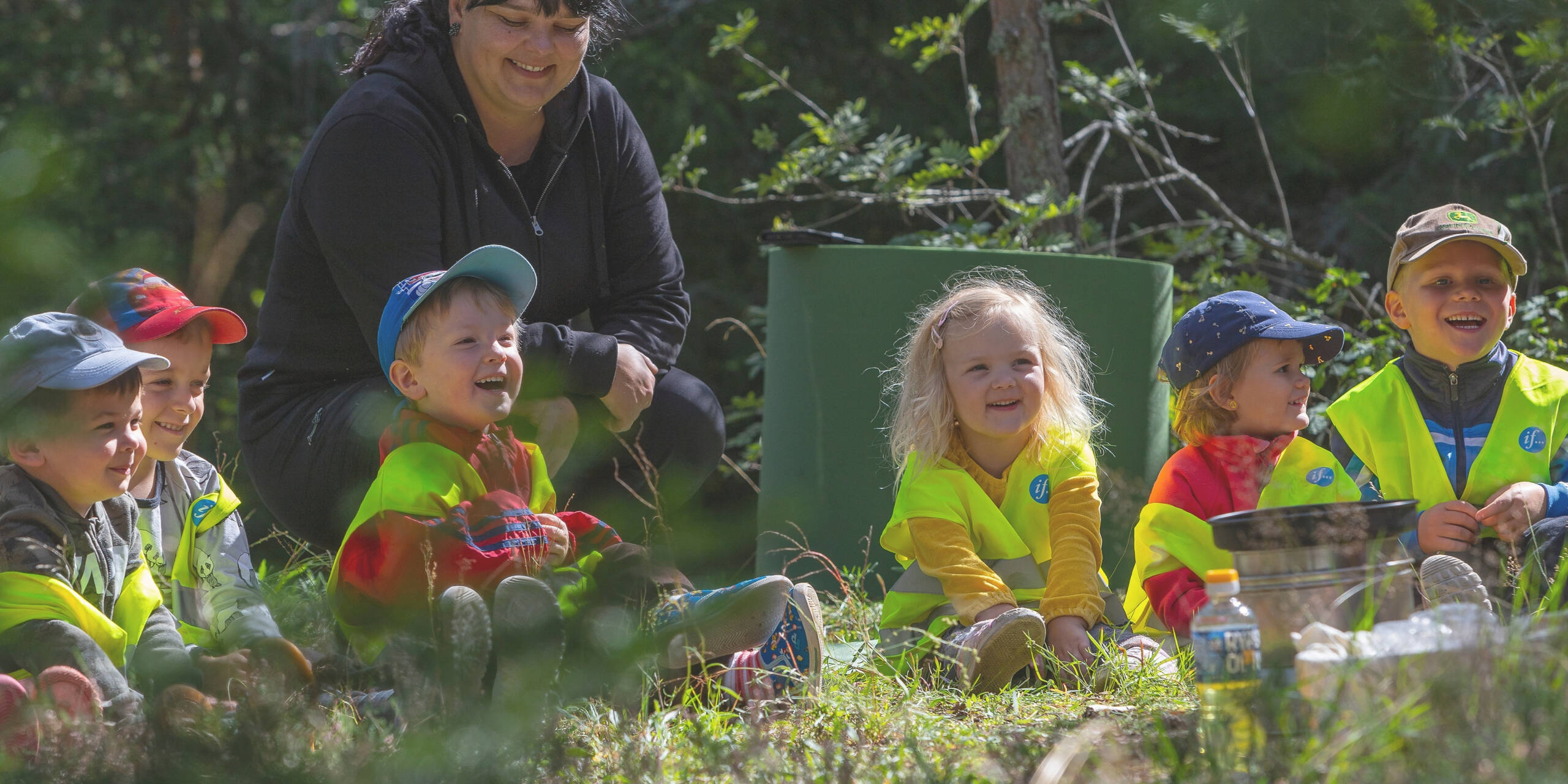 Lapset istuvat nurmikolla hymyillen ja katsoen samaan suuntaan.