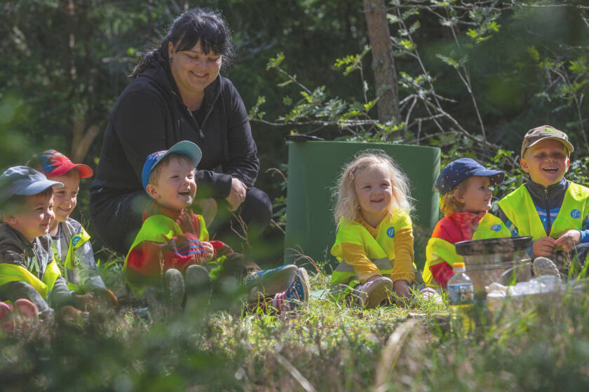 Lapset istuvat nurmikolla hymyillen ja katsoen samaan suuntaan.
