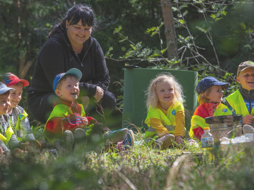 Lapset istuvat nurmikolla hymyillen ja katsoen samaan suuntaan.