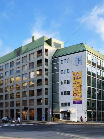Moderni, tummanharmaa kerrostalo kahden kadun risteyksessä.