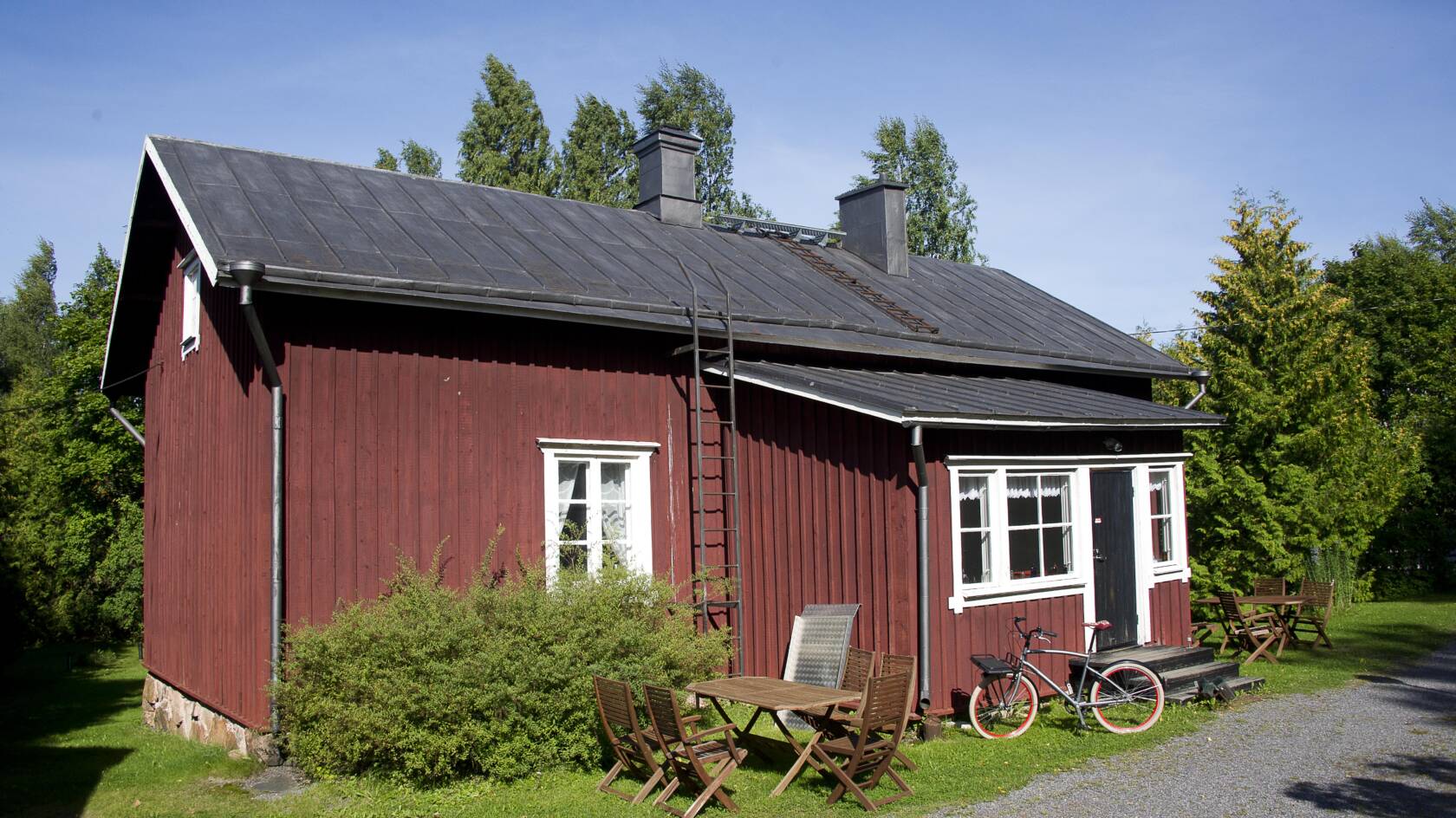 Vanha punainen puurakennus, jossa on ruutuikkunat. Edustalla pöytä ja tuoleja sekä polkupyörä.