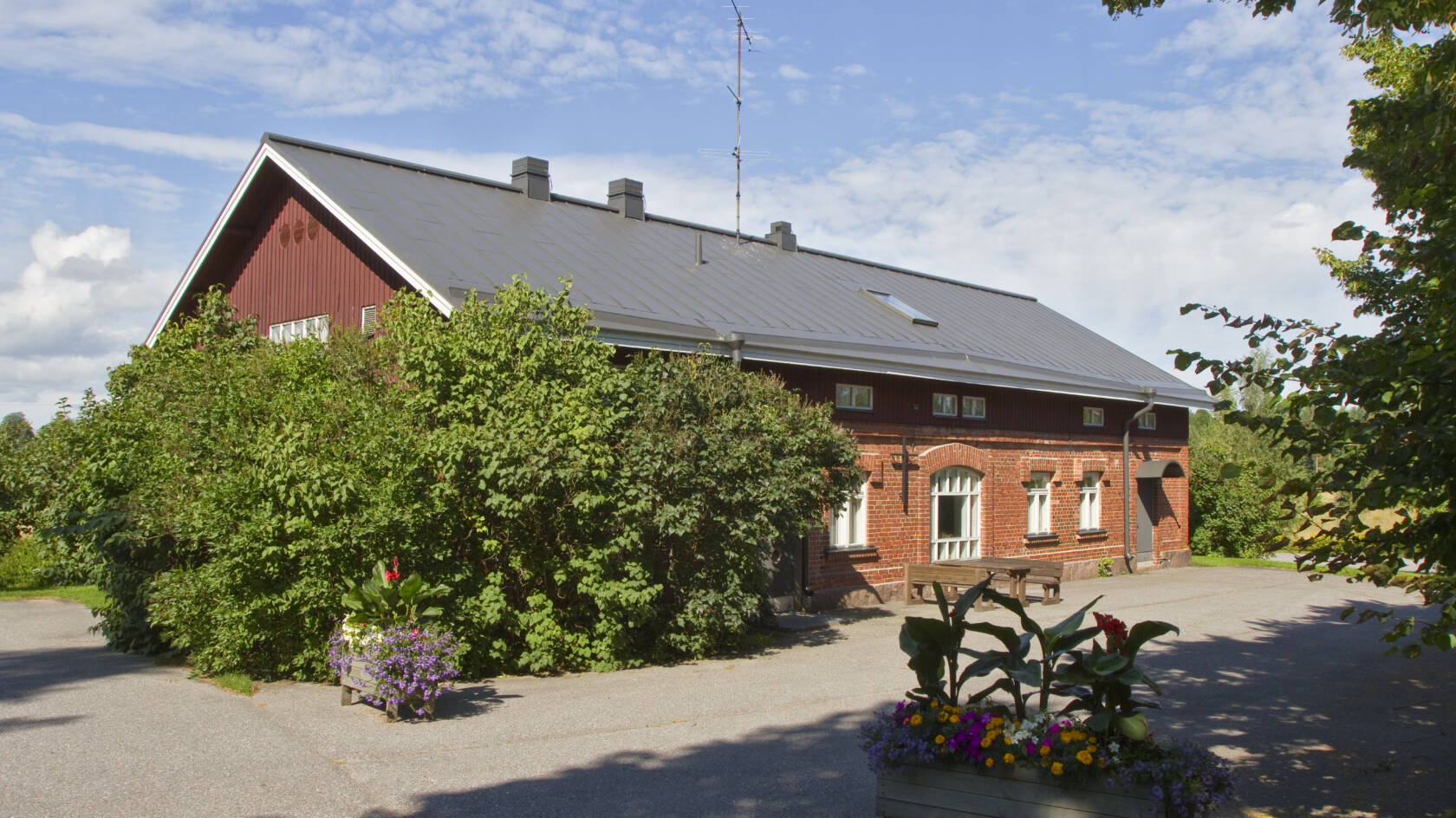 Punatiilinen rakennus, jonka edustalla kasvaa isoja syreenipensaita.