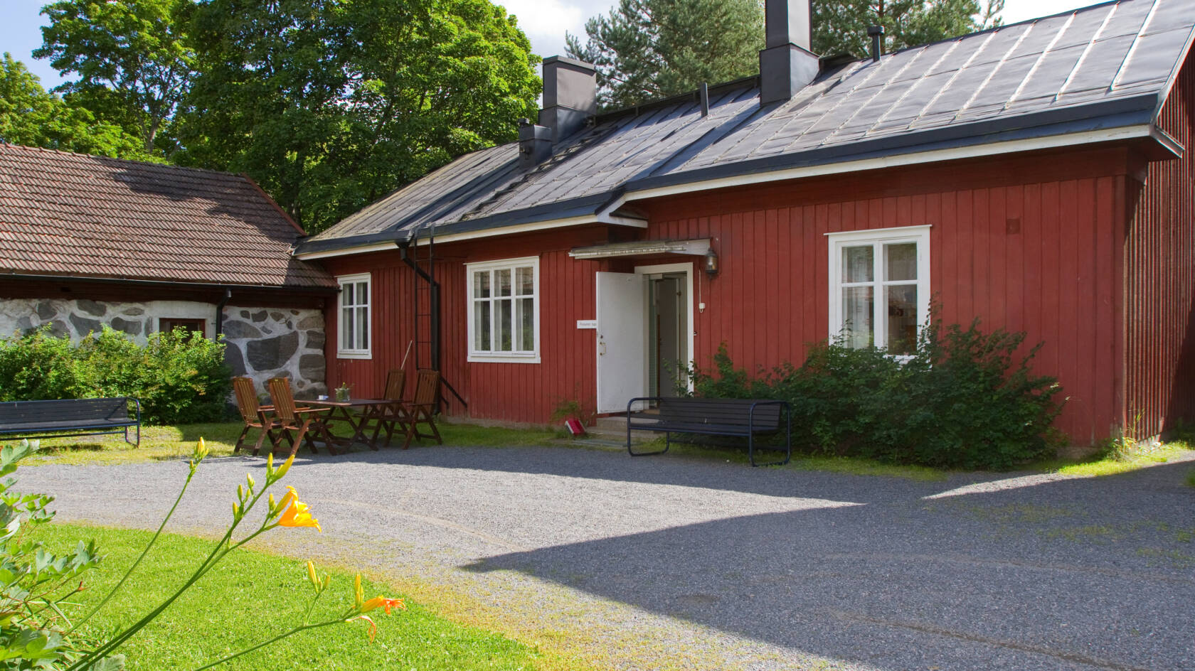 Vanha punainen puurakennus, jonka edustalla penkki ja pöytäryhmä.
