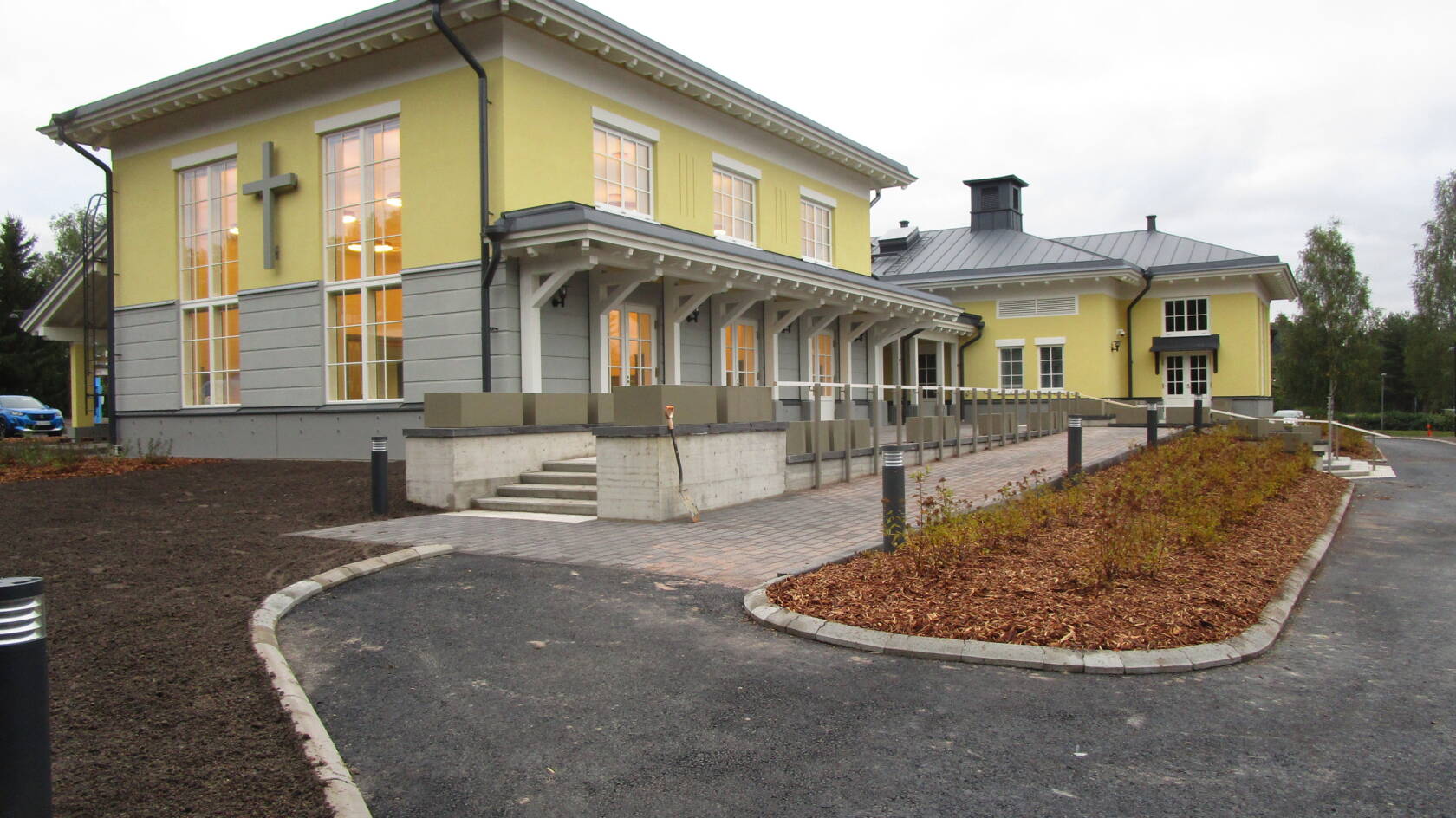 Kelta-harmaa uusi rakennus, jossa korkeat ruutuikkunat. Edustalla laatoitusta ja istutusalue.