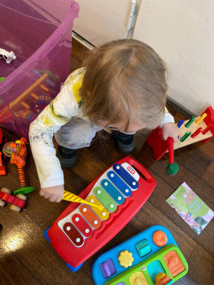 En liten flicka sitter på huk och spelar på en xylofon.