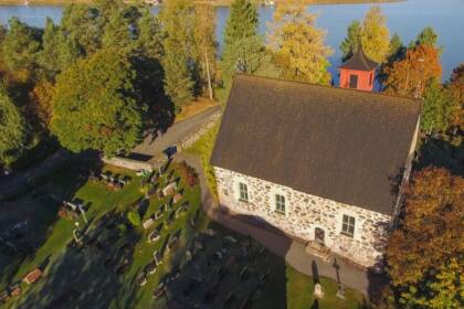 Pieni kivikirkko ja sitä ympäröivä hautausmaa kylpee nousevan auringon valossa ilmasta käsin kuvattuna.
