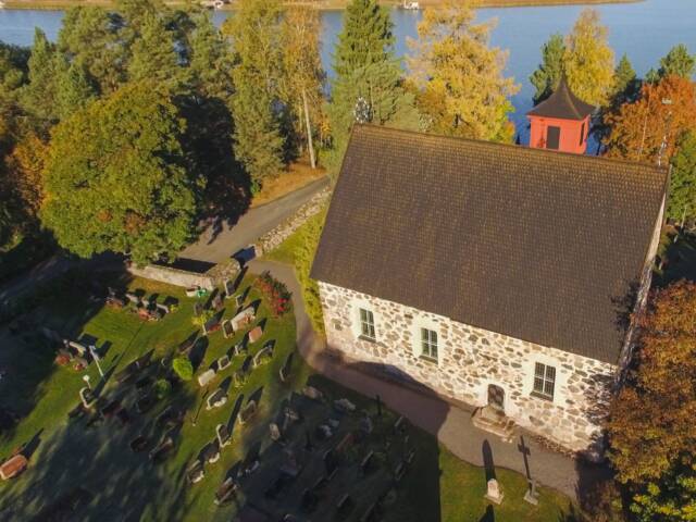 Pieni kivikirkko ja sitä ympäröivä hautausmaa kylpee nousevan auringon valossa ilmasta käsin kuvattuna.