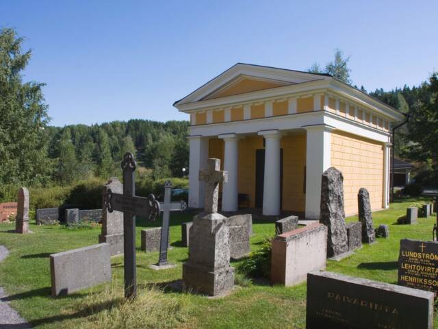 Kelta-valkoinen, empire-tyylinen hautakappeli pylväineen keskellä hautausmaata.
