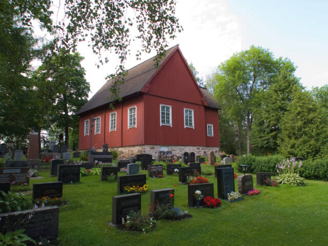 Punainen puinen kirkko hautausmaan keskellä.