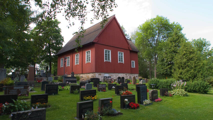 Punainen puinen kirkko hautausmaan keskellä.