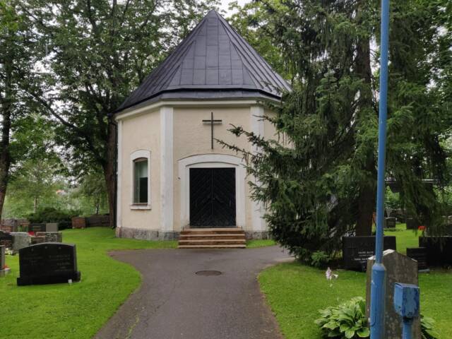 Hautausmaan keskellä on valkosävyinen pieni rakennus, jonka oven päällä on risti.