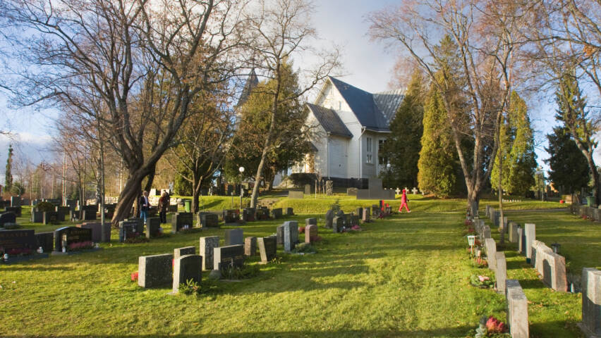Valkoinen kirkko ja sen ympärillä oleva syksyinen hautausmaa.