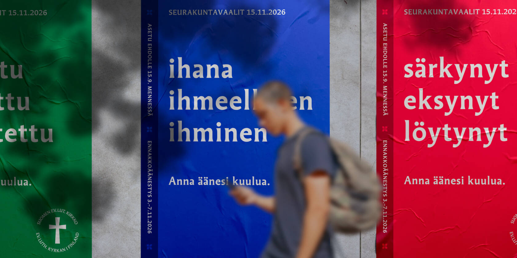 Kolme julistetta seinällä, joissa on eri värejä ja tekstejä. Henkilö kävelee ohi, taustalla näkyy punainen, sininen ja vihreä juliste.