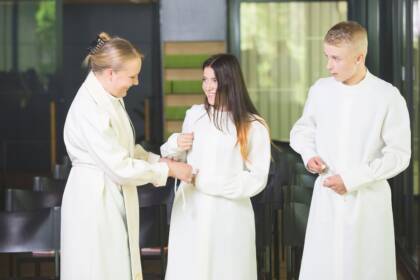 Pappi auttaa tyttöä solmimaan alban vuon. Vieressä seisoo poika.
