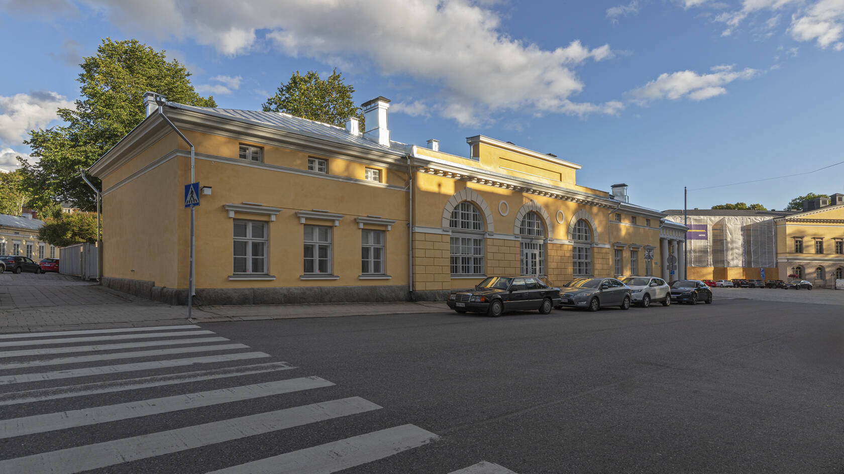 Keltainen kivirakennus, jonka keskellä on kolme isoa kaari-ikkunaa ja molemmilla sivuilla kolme ruutuikkunaa.