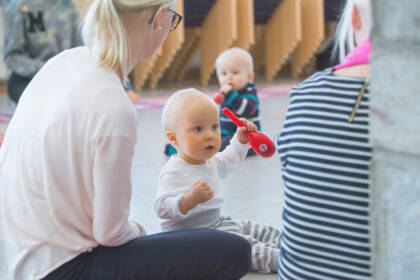 Kaksi aikuista ja kaksi vauvaa istuu lattialla. Vauvojen käsissä on marakassit.