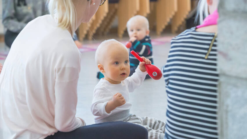 Kaksi aikuista ja kaksi vauvaa istuu lattialla. Vauvojen käsissä on marakassit.