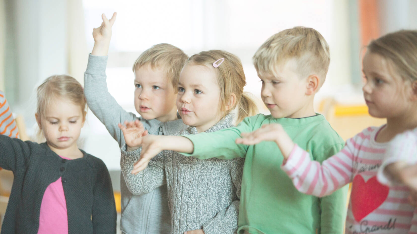 Viisi lasta seisoo rivissä ojennellen käsiään.