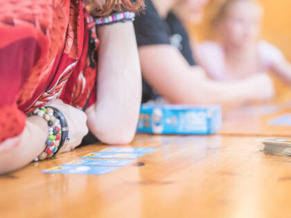 Pöydälle on levitetty pelikortteja ja ihmisiä on nojautunut pelaamaan.