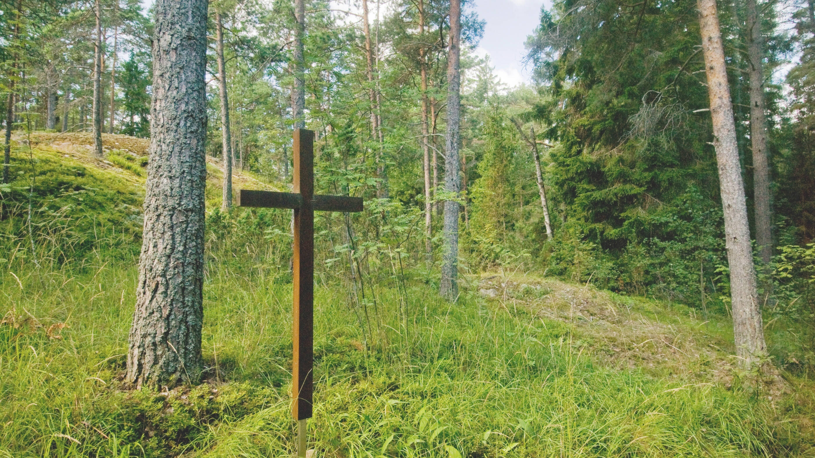 Metallinen risti keskellä vehreää metsää.