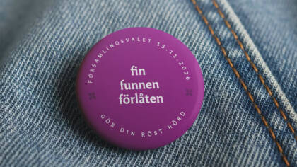 Lila knapp på denimtyg, texten "fin funnen förlåten" och datumet 15.11.2026.