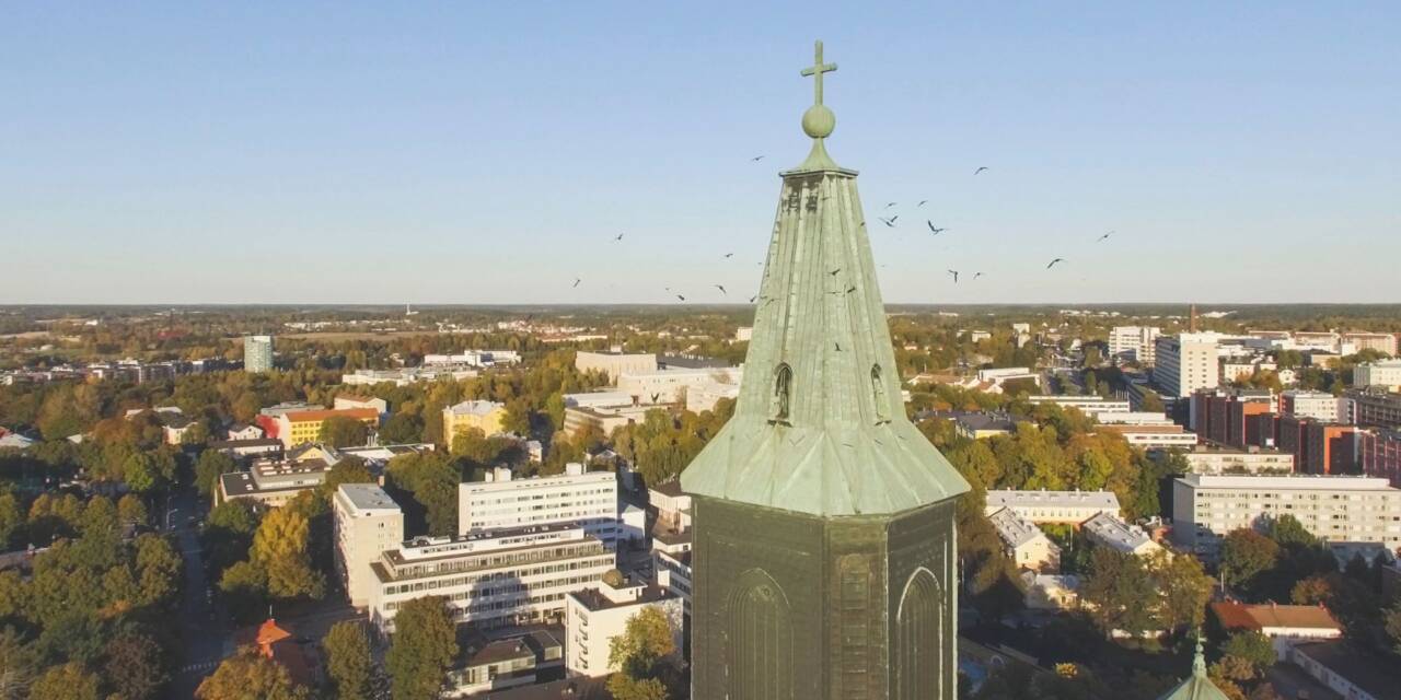 Linnut parveilevat Tuomiokirkon tornin ympärillä, taustalla näkyy kaupunkia.
