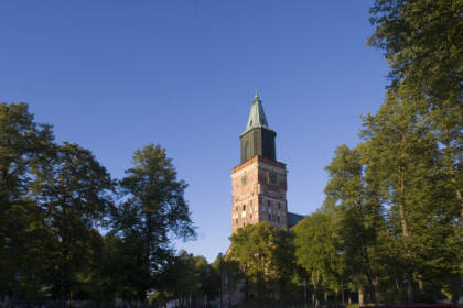 Turun tuomiokirkon torni sinistä taivasta vasten, ympärillä vihreitä puita ja kirkon vanha rakennus.