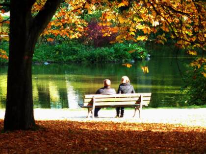 två vuxna som sitter på en parkbänk vid ån på hösten.